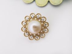 a pearl and diamond brooch sits on a white surface next to a green flower