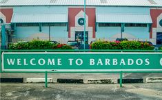 a welcome to barbados sign in front of a building with cars parked outside