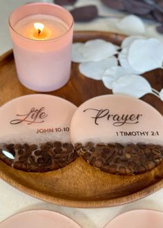 two personalized coasters sitting on top of a wooden plate next to a candle