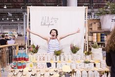 a woman standing in front of a table with lots of jars and plants on it