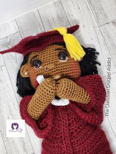 a crocheted doll is laying on the floor wearing a red sweater and yellow hat