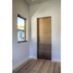 an empty room with a wooden door and window on the wall, next to a hard wood floor