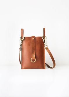 a small brown leather bag on a white background with a gold ring around the strap