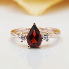 a close up view of a ring with a red stone and two diamonds on it