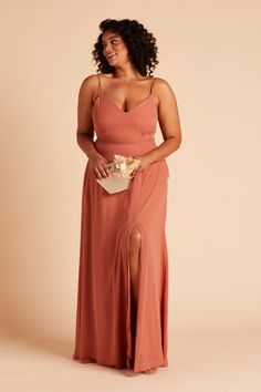 a woman in an orange dress is holding a white purse and posing for the camera