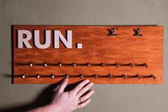 a person holding up a wooden sign with the word run on it and several hooks attached to it