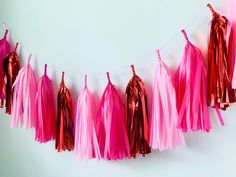 pink and red tissue tassels hanging from a string on a white wall,