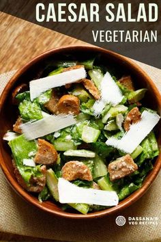 a wooden bowl filled with salad on top of a table next to a fork and knife