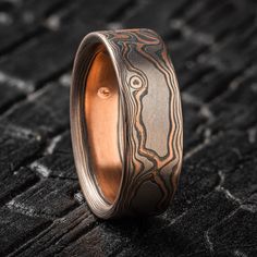 "* Price may vary depending on ring size, please inquire with us directly with your needed size for accurate pricing! This beautifully rustic Mokume Gane wedding ring features a woodgrain pattern and a flat profile in a 7mm width. It is made with our \"Embers\" metal combination that features 14k red gold, Palladium, and sterling silver with an etched and oxidized finish.  Pattern: Woodgrain  Palette: Embers  Finish: Etched & Oxidized Profile: Flat Width Shown: 7mm Size Shown: 9.25 Add On: Palladium Top Sheet Price does NOT include stones or setting fees. We care about customer service and would like to hear from you! Please contact us to help create your treasured item, we take your concerns and requests to heart and will work together to create your unique designs SPECIAL PRICING FOR SET Round Patina Rings For Anniversary, Rustic Adjustable Etched Jewelry, Artisan Patina Rings For Anniversary, Rustic Ring For Anniversary, Handmade Brown Ring For Wedding, Artisan Etched Jewelry For Wedding, Rustic Anniversary Jewelry Ring, Rustic Brown Engraved Jewelry, Artisan Engraved Wedding Rings