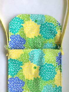 a colorful flowered bag is hanging on a white surface with yellow straps and two green buttons