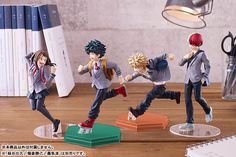 figurines of anime characters are posed in front of a desk with books and office supplies