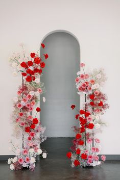 an arch made out of flowers and branches in front of a white wall with a doorway