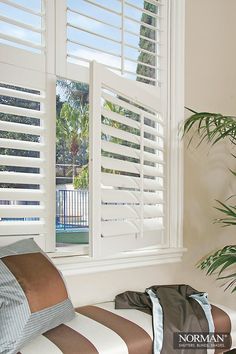 a window with white shutters and a striped pillow on it next to a potted plant