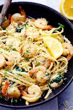 pasta with shrimp and spinach in a pan next to lemon wedges on the side