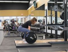 a woman squats on a barbell in a gym with other people working out