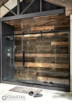 a wooden shower stall with glass doors and wood planks on the walls, along with a black tiled floor