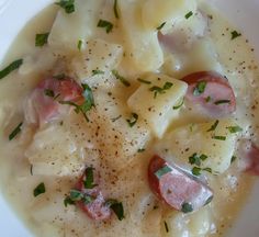 a white bowl filled with pasta and ham on top of a wooden table next to a fork