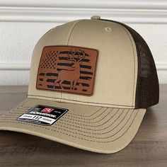 Deer Hunting American Flag Patriotic Leather Patch Hat Khaki/Brown. Specifications: 🧢 Richardson original 112 trucker; adjustable for the perfect fit 🎩 60/40 cotton/polyester blend for comfort 📏 One size fits most 🏷️ Expertly laser engraved leatherette patch design 📦 Ships in 2 to 3 business days from our Orlando Studio Care Instructions: 🚫 Do not wash; spot clean only Please Note: 🌈 Colors may vary from photos based on your viewing screen. Brown Military Hat, One Size Fits Most, Brown Military Visor Hat, Brown Military Hat With Curved Brim, Military Style Brown Hat With Curved Brim, Brown Winter Snapback Hat, Brown Military Style Trucker Hat, Brown Military Trucker Hat, Brown Winter Trucker Hat, Brown Military Hat For Outdoor