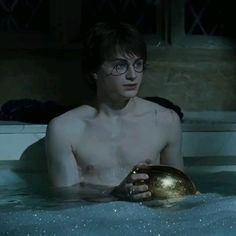 a shirtless young man holding a golden ball in a hot tub with bubbles on it