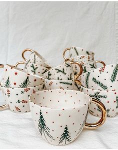 a group of christmas themed cups and saucers on a white tablecloth with gold rims