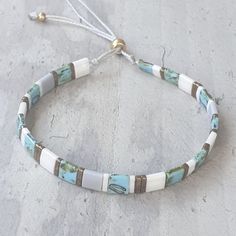 a white and blue beaded bracelet sitting on top of a cement floor next to a string