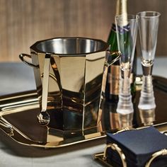 there is a gold plate with two glasses and a bottle on the table next to it