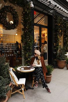 a woman sitting at a table in front of a store with christmas decorations on the windows