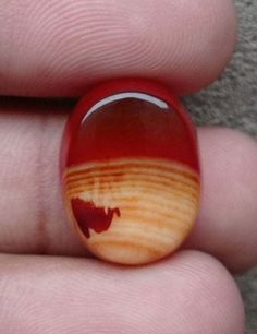 a hand holding a red and brown glass ring