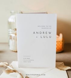 a white wedding card sitting on top of a table next to some flowers and candles