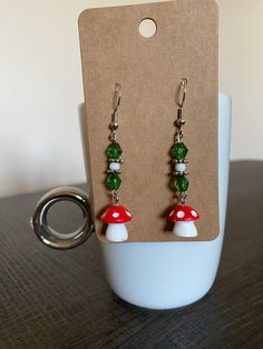 Adorable and trendy handmade mushroom drop earrings! Made with cute Fairycore mushroom charms paired with green beads. Simple and tasteful!  * All materials were cleaned and sanitized prior to use and kept in a clean smoke free environment. Comes packaged in a mesh bag. Whimsical Green Jewelry With Mushroom Design, Green Mushroom Design Dangle Earrings, Adjustable Green Mushroom Design Earrings, Green Adjustable Mushroom Design Earrings, Adjustable Green Earrings With Mushroom Design, Green Dangle Earrings With Mushroom Design, Whimsical Green Mushroom Earrings, Whimsical Green Mushroom Design Earrings, Cute Mushroom Design Dangle Jewelry