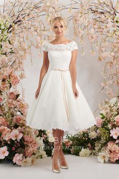 a woman standing in front of flowers wearing a white dress with lace overlays