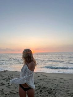 a woman standing on top of a sandy beach next to the ocean at sun set