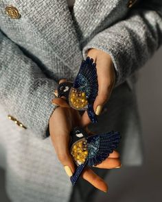 the woman is holding two small birds in her hands, both with yellow and blue decorations on their fingers