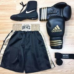 a pair of black and gold adidas boxing gloves, booties, and headgear laid out on a wooden floor