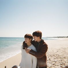 two young men standing on the beach next to each other