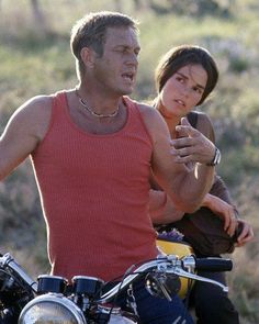 a man and woman riding on the back of a motorcycle in front of a field