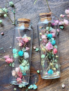 two glass jars filled with flowers sitting on top of a wooden table next to each other