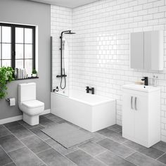 a white bathroom with grey tile flooring and walls, along with a plant in the corner