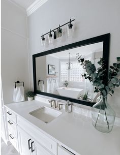 a bathroom vanity with a large mirror above it and a vase filled with flowers on the counter