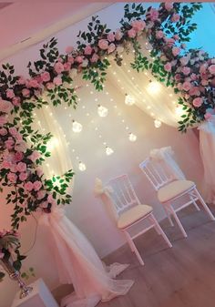 a room decorated with white chairs and pink flowers on the wall, lights in the background