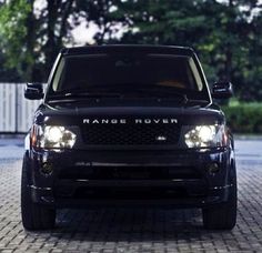 the front end of a black range rover parked on a cobblestone road with trees in the background