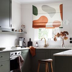 a kitchen with green cabinets and an orange patterned roman blind in the window over the sink