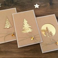 three christmas cards with gold foil trees on them and string tied around the edges, sitting on top of a wooden table