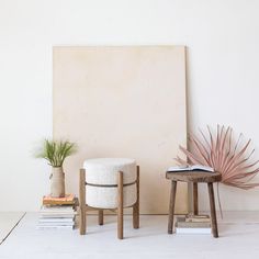 two stools and a plant in front of a white wall with a book on it