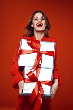 a woman in a red dress is holding a white gift box with a red ribbon on it