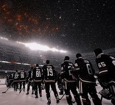 a group of hockey players standing on top of a snow covered field in front of an ice rink