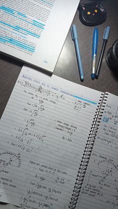 an open notebook with writing on it next to some pens and a calculator