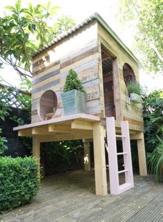 a small wooden house made out of pallet boards and other wood material with potted plants on the roof