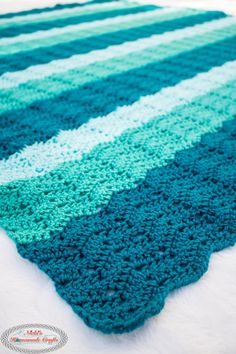 a blue and green crocheted rug on top of a white bed coverlet