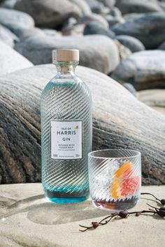 a bottle of harris gin next to a shot glass on the sand at the beach